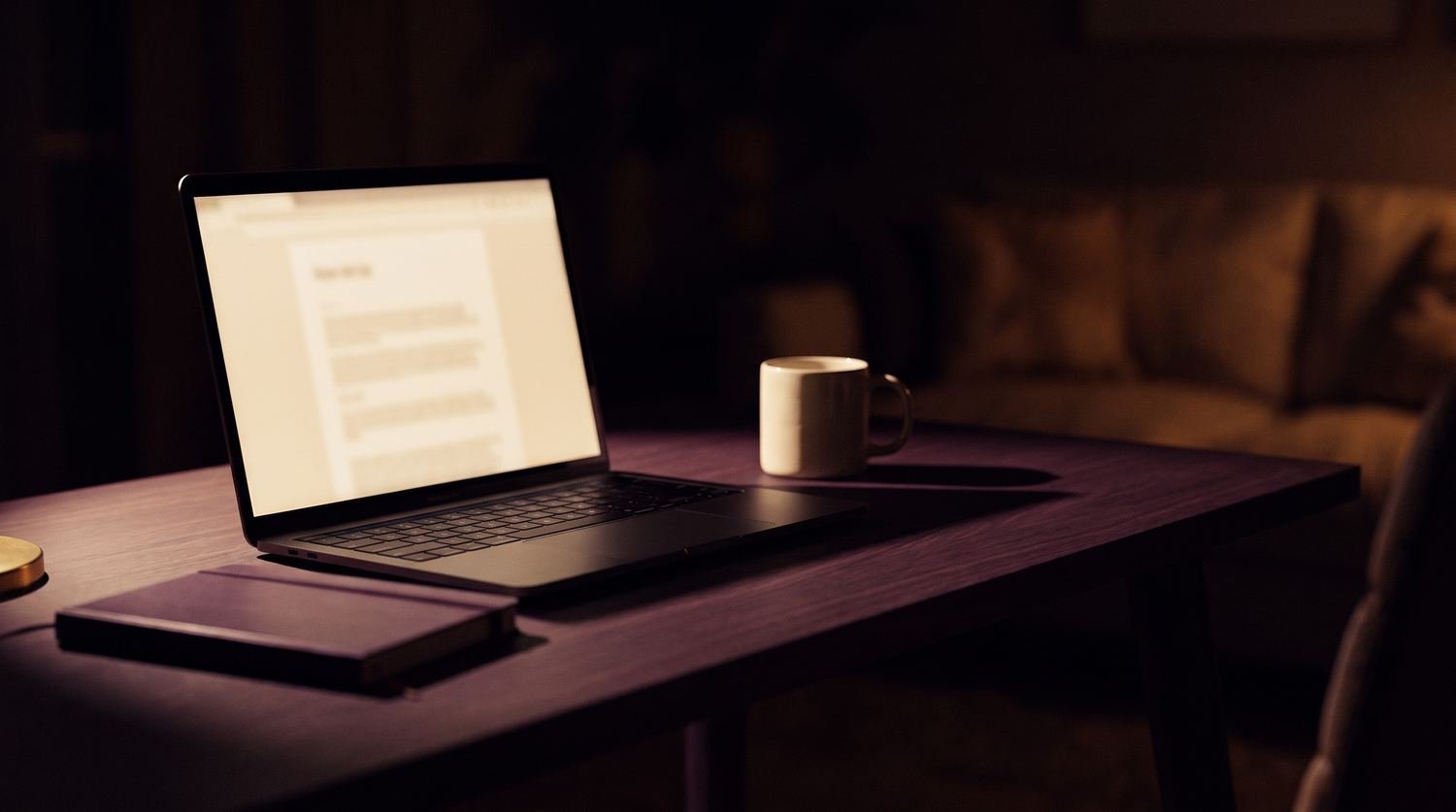 Un ordinateur portable ouvert sur un bureau, tard le soir, dans une pièce sombre.